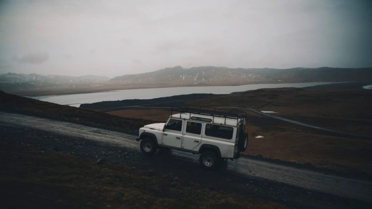 White SUV driving on a dirt road above a lake