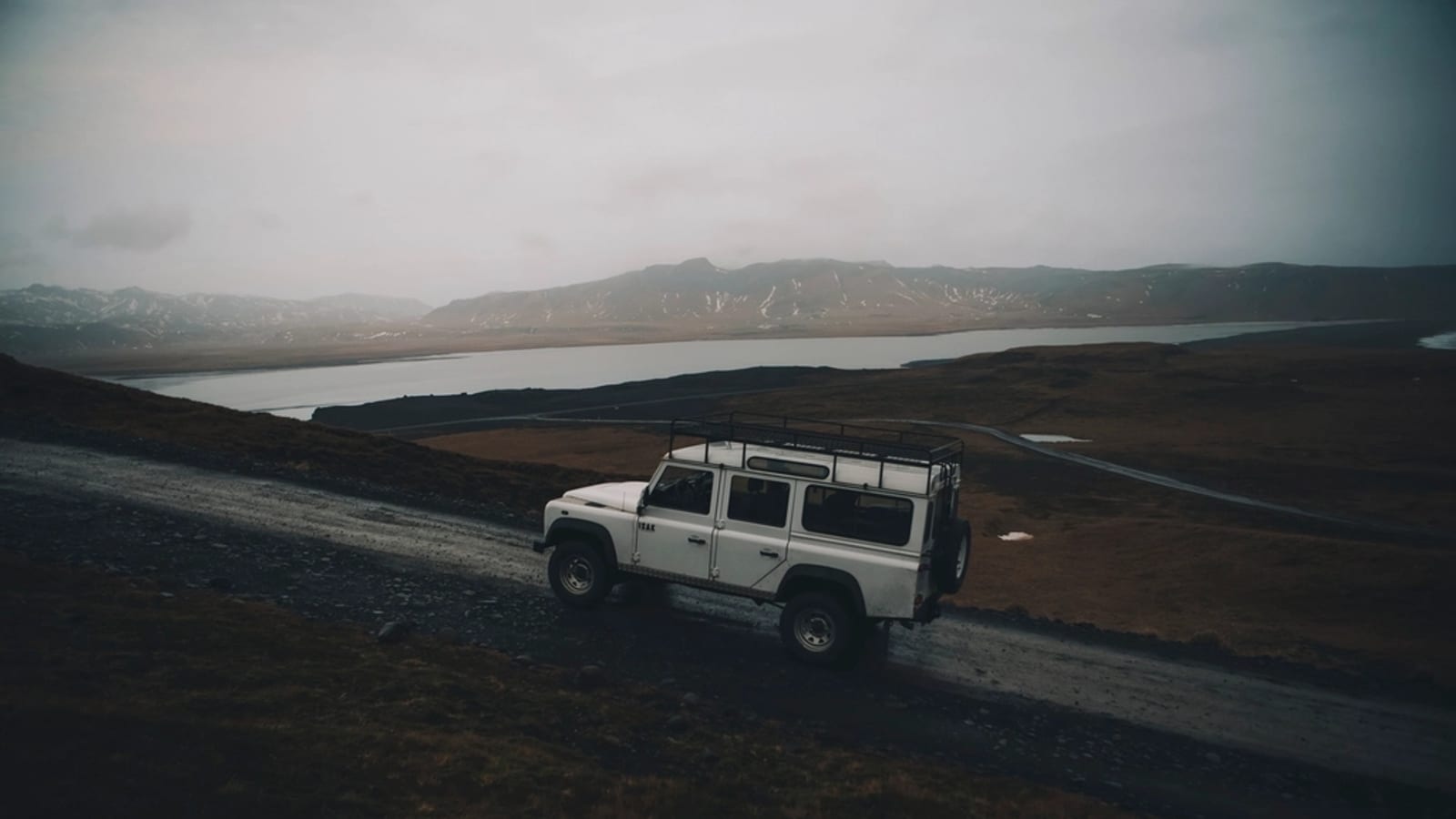 White SUV driving on a dirt road above a lake