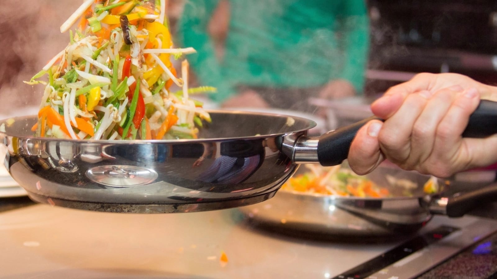 Vegetables being tossed in a stainless steel frying pan