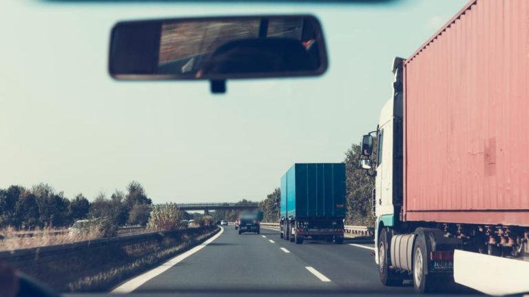 Semi trucks on a multi lane highway seen through a car windshield